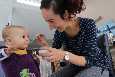 Eine Mutter füttern ihr Kleinkind mit Babybrei aus einer Tasse