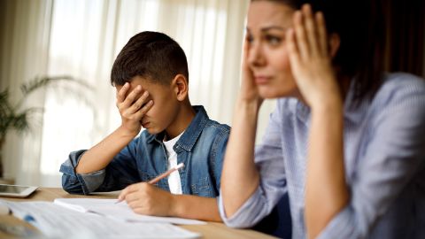 Mère et fils ayant l’air stressé sont assis à une table en train de faire les devoirs
