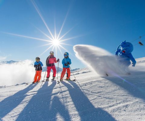 Mascotte spruzza con la neve tre bambini sugli sci