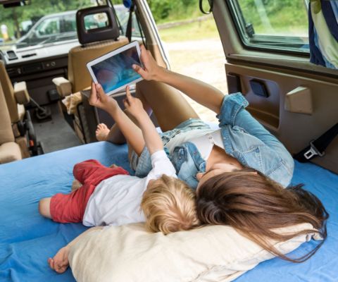 Mutter und kleines Kind liegen im Auto mit einem Tablet-PC