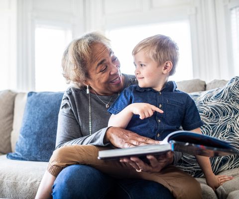 Une grand-mère assise sur le canapé en train de regarder un livre avec son petit-enfant