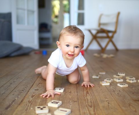 Baby krabbelt über einen Holzfussboden mit Holzspielzeug