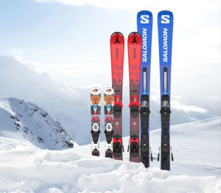 Trois paires de skis plantés dans la neige devant un paysage hivernal