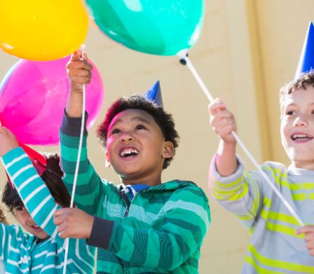 Trois garçons tenant des ballons de baudruche en l’air à leur fête d’anniversaire