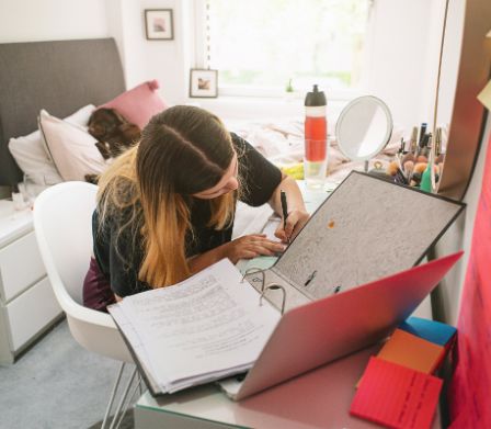 Une adolescente est assise à son bureau avec un classeur ouvert et écrit