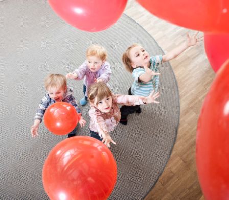 Kleinkinder spielen mit roten Luftballons