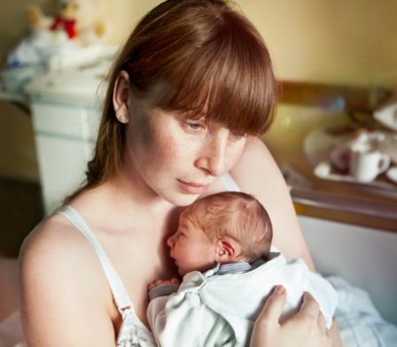 Mutter schaut melancholisch mit Baby im Arm