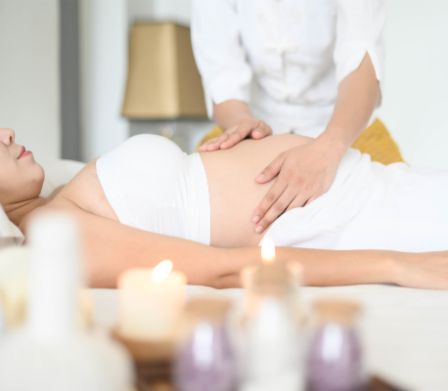 Donna incinta sorridente mentre si fa massaggiare il pancione
