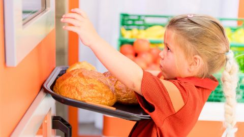 Una bambina mette il pane nel forno della mini Migros