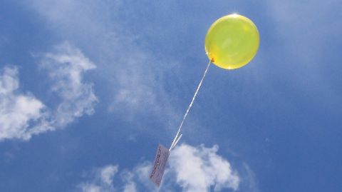 Gelber Luftballon mit einer Karte steigt in den blauen Himmel