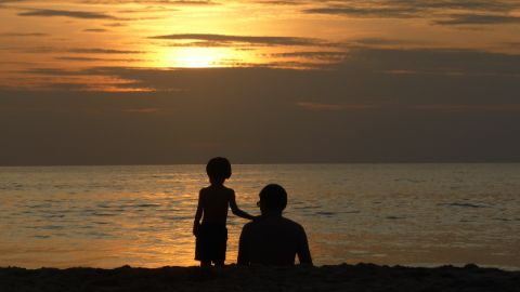 Silhouette d’un père et de son fils devant un coucher de soleil sur la mer Silhouette d’un père et de son fils devant un coucher de soleil sur la mer