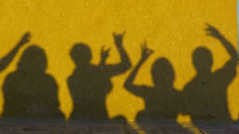 Famille jouant au jeu des ombres chinoises devant un mur jaune Famille jouant au jeu des ombres chinoises devant un mur jaune