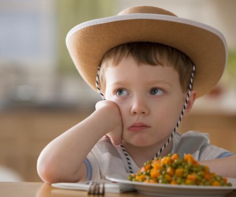 Un garçon avec un chapeau de cow-boy assis devant une assiette et ne veut pas manger.