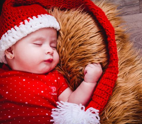 Un bebè addormentato con un vestitino bianco e rosso e una cuffietta 