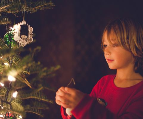 Junge hängt Kugel am Weihnachtsbaum auf