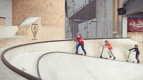 Drei Kinder fahren im Rolling Rock mit dem Trottinett umher.