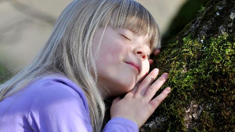 Mädchen lauscht an Baumstamm
