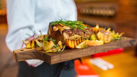 Eine Frau serviert auf einem Holzbrett ein grosses Stück Grillfleisch und Gemüse Eine Frau serviert auf einem Holzbrett ein grosses Stück Grillfleisch und Gemüse