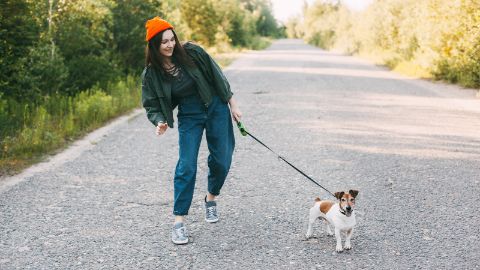 Giovane donna va a passeggio con un cagnolino al guinzaglio