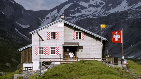 Capanna del CAS con bandiera svizzera sventolante davanti a montagne innevate