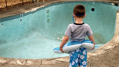 Kleiner Junge mit Schwimmring steht vor einem leeren und dreckigen Pool