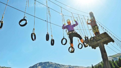 Frau klettert in einem Parcours mit Ringen im Seilpark Pradaschier Frau klettert in einem Parcours mit Ringen im Seilpark Pradaschier