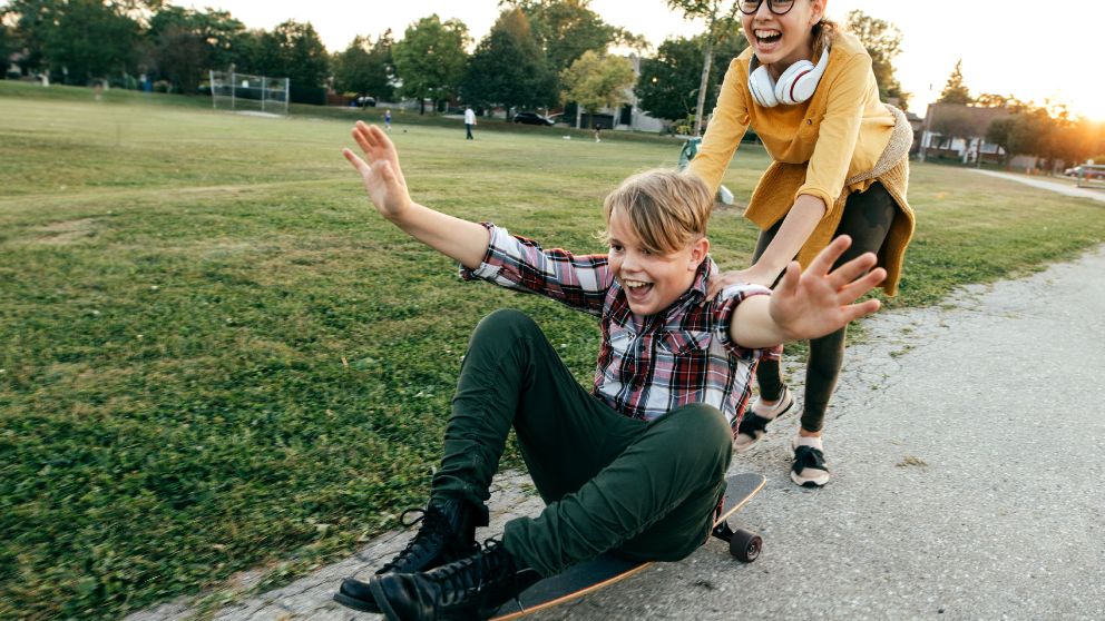 Une fillette rieuse pousse un garçon assis sur un skate-board