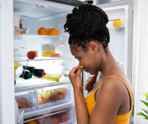 Une femme se bouche le nez devant un réfrigérateur ouvert