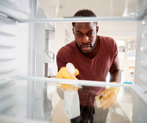 Uomo intento a pulire il frigorifero con apposito detergente e spugna