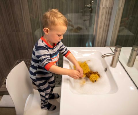 Un bambino lava il suo peluche nel lavandino