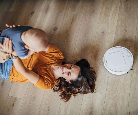 Mutter mit Kind spielen auf dem Boden mit Staubsaugerroboter