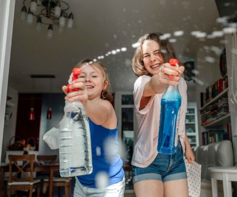 Zwei fröhliche Mädchen putzen streifenfrei die Fenster