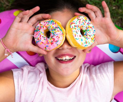 Une fillette tenant deux donuts au sucre devant ses yeux.