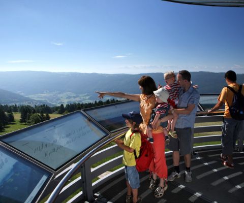 Famille sur une tour panoramique avec panneaux d’information indiquant les montagnes aux alentours