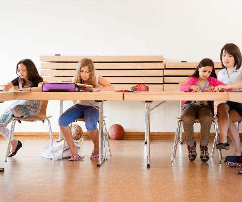 Drei Kinder und Lehrerin sitzen an Schulbank