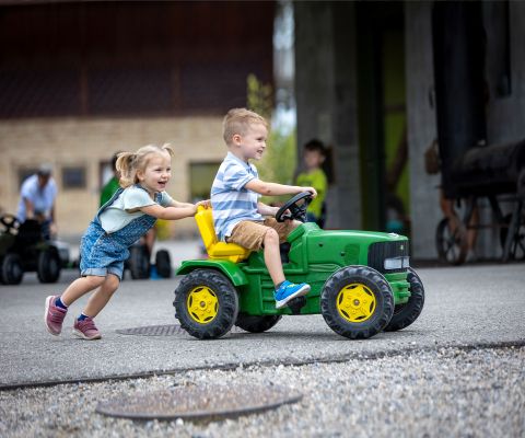 Un garçon sur un mini-tracteur rit en se faisant pousser par une fillette