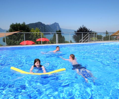 Famille dans une grande piscine avec un lac et les montagnes en arrière-plan