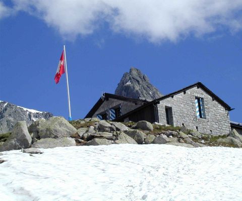 Vista esterna della capanna da l’Albigna del CAS con una bandiera svizzera e neve in primo piano