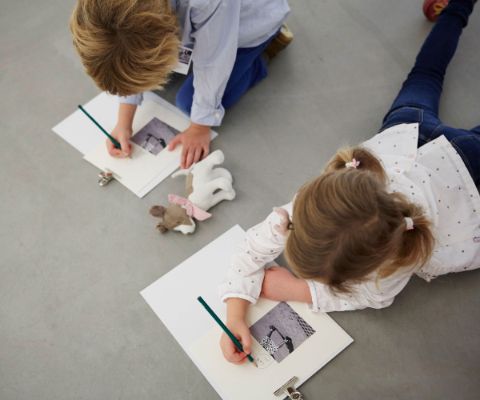 Zwei Kinder liegen am Boden und schreiben etwas über ein Foto