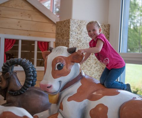 Parco giochi indoor Appenzellerpark a Herisau: un bambino cavalca una grande mucca giocattolo