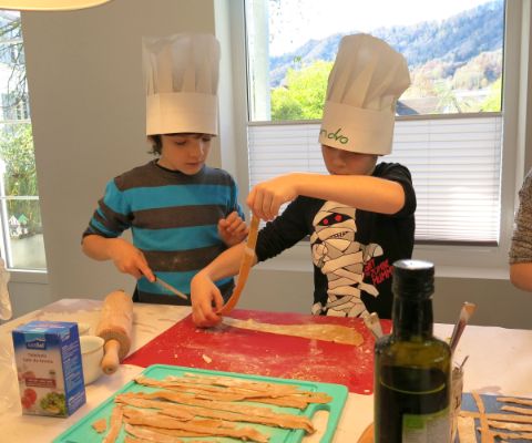 Zwei Kinder mit Kochhüten üben sich im Pasta selber machen