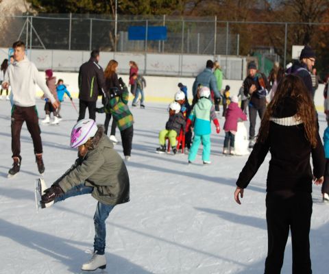 Kinder und Erwachsene am Schlittschuhlaufen auf einer Eisbahn im Freien