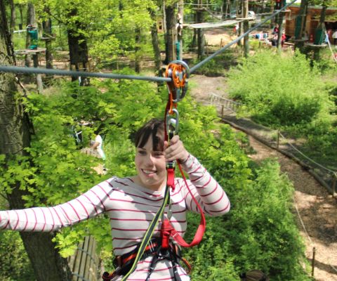 Mädchen an Kletterseilen hoch in den Bäumen im Parc Aventure Genf