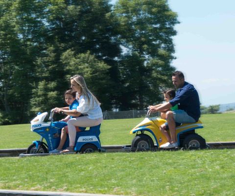 Familie fährt auf zwei kleinen Motorrädern auf einer Bahn im Miniland