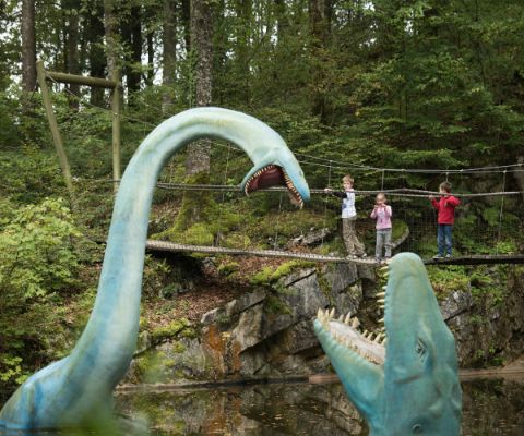Kinder schauen von einer Brücke auf zwei kämpfende Dinosaurier in einem See