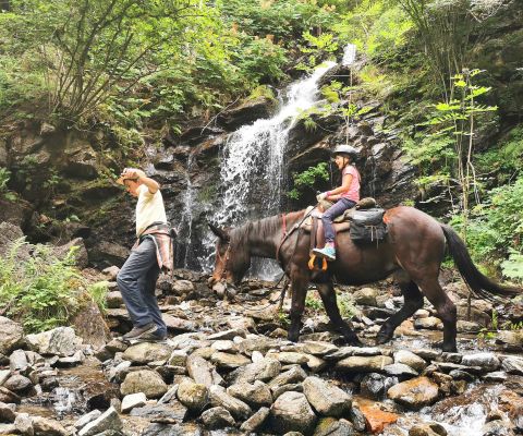 Mann läuft vorsichtig über einen steinigen Pfad, Kind reitet dahinter auf einem Pferd