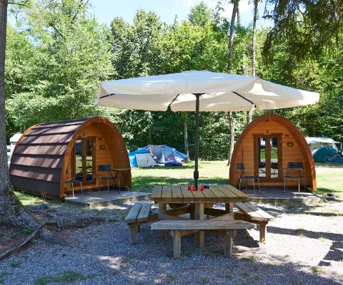 Kleine Holzhütten davor Tisch mit Bänken und Zelten im Hintergrund
