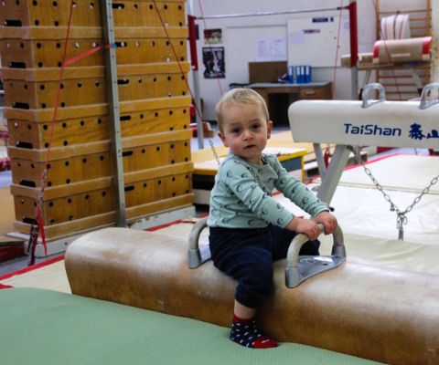 Kleiner Junge sitzt auf Turnbalken