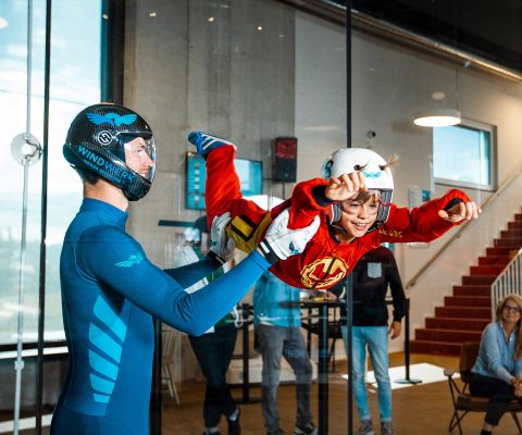 Ein Junge schwebt wie ein Superhero in der Flugkammer, gehalten vom Instruktor