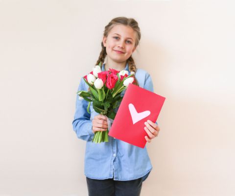 Mädchen hält Muttertagskarte mit Herz und Blumenstrauss in der Hand
